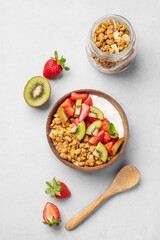 Natural yogurt with granola, kiwi and strawberries in a wooden bowl on a light background with fresh berries and fruits.