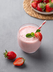 A glass of fresh strawberry smoothie with mint on a blue background with fresh berries.