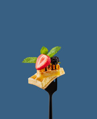 Wafer pieces with fresh strawberries, blackberries, mint leaves  on a black fork on a blue...