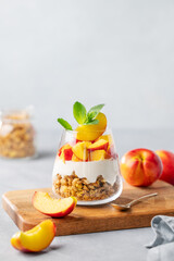 Greek yogurt parfait with peach and granola in a glass on a wooden board on a light background with...