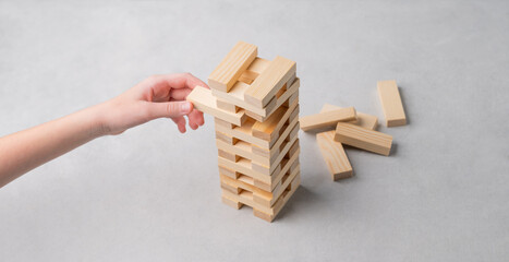 A hand pulls out a piece from a wooden tower game on a light background.