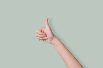 Hand shows thumb up on a light green background. Sign language concept ok.