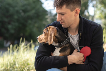 Image of young man smiling and sitting with his beagle dog in park in the morning