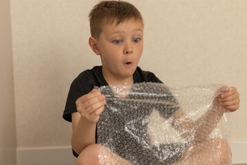 Surprised boy popping bubble wrap indoors. Close-up image