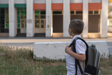 A young schoolboy outside in front of his school turns around and looks at his school