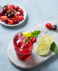 Cherry-lime mojito cocktail with mint, lime and ice on a marble board on a blue background.