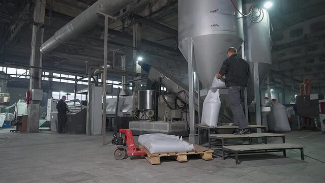 Worker opening the white bags in front of the factory tank. Plant worker emptying the bag into the tank container. Worker pours the bag with material into the recycling tank. Production.
