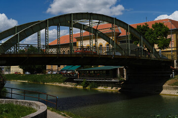 A small iron arch bridge over the river, on which cars and pedestrians drive. The canal is in the...