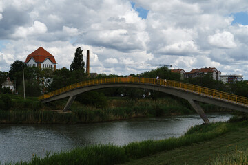 An arched pedestrian bridge over the river. Residential buildings with red tiled roofs. A small town in Serbia is Zrenjanin. Vojvodina District.