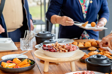 People enjoying a buffet-style meal, serving themselves from a variety of dishes including appetizers and snacks, creating a casual and inviting atmosphere for social dining.