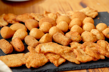 An inviting platter of assorted fried snacks, including golden-brown croquettes, chicken strips, and cheese balls, perfectly arranged on a slate board, ready to be enjoyed at a social gathering.