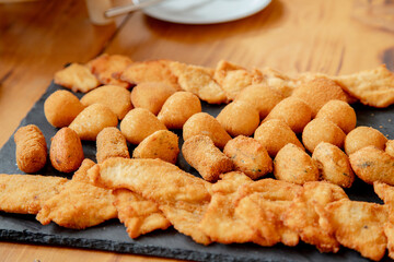 An inviting platter of assorted fried snacks, including golden-brown croquettes, chicken strips, and cheese balls, perfectly arranged on a slate board, ready to be enjoyed at a social gathering.