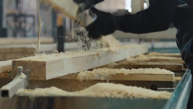 Laborer is taking out the wooden plank pieces from workbench. Worker is throwing away waste after cutting wooden plank. Worker is cleaning processed wooden plank from excess shavings