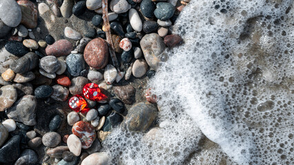 Red playing dice among gray stones and foam from the sea wave.