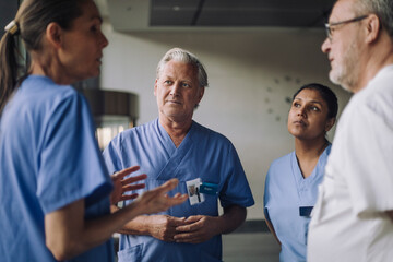 Happy male and female doctors in medical scrubs discussing at hospital