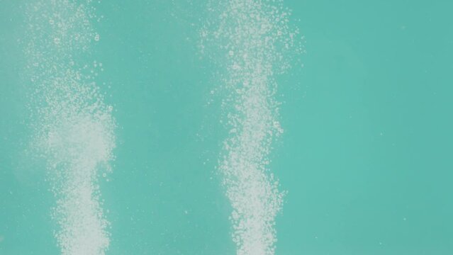 The pair of white effervescent pills on a turquoise background lie at the bottom of the container and dissolve in water to form bubbles and powder. The concept of testing medical drugs in the