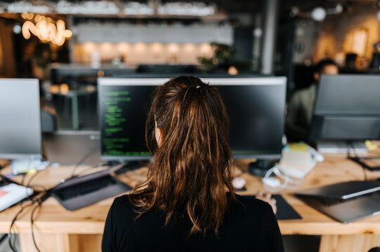 Rear of female coder with ponytail sitting at desk in office