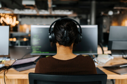 Rear view of female computer programmer with headphones doing coding at tech start up at office
