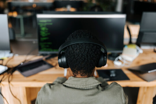High angle view of male computer programmer wearing headphones and coding at office