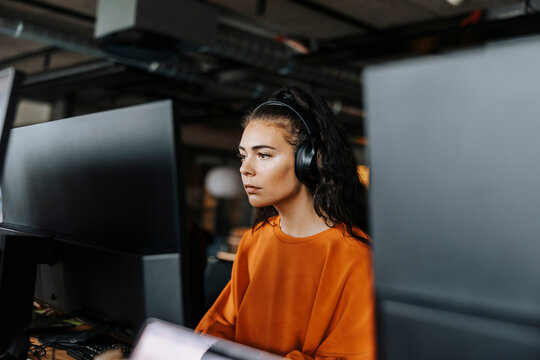 Focused female computer programmer with wireless headphones working at office