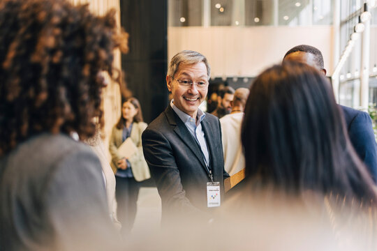 Happy senior male entrepreneur talking with delegates during networking event at convention center