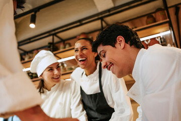 Low angle view of young male chef enjoying with coworkers in commercial kitchen