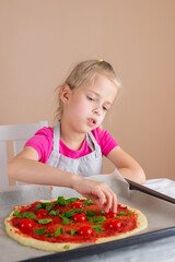 Beautiful girl is preparing pizza, she spreads tomatoes and herbs on the dough. Yeast-free pizza, homemade, handmade, DIY pizza. Vertical orientation.