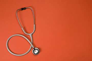 Stethoscope on crimson background, top view. Space for text