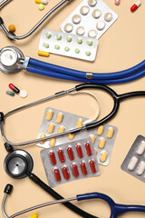Stethoscopes and pills on beige background, flat lay. Medical tools