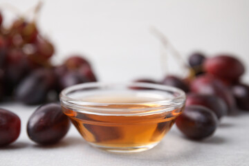 Wine vinegar in glass bowl and grapes on light grey table, closeup