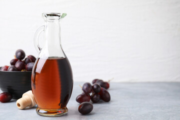 Wine vinegar in glass jug and grapes on grey table, space for text