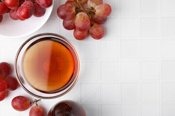Wine vinegar in glass bowl and grapes on white tiled table, flat lay. Space for text