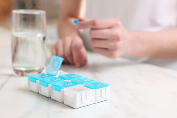 Woman with pills, organizer and glass of water at white marble table, selective focus