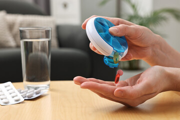 Woman with pills, organizer and glass of water at light wooden table, closeup