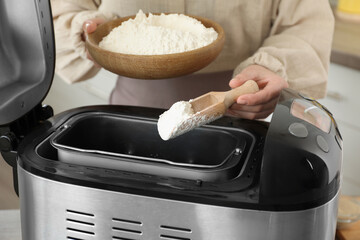 Making dough. Woman adding flour into breadmaker machine, closeup