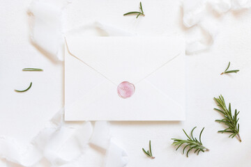 Blank sealed envelope near white silk ribbons and rosemary leaves top view, wedding mockup