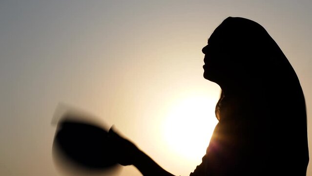 A woman sitting under the hot sun tries to cool her body using a hand fan.