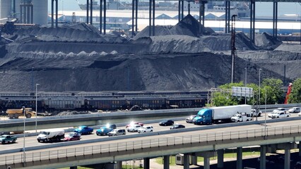 Shipyard beside interstate highway with cars traveling past coal refinery and boats in harbor 