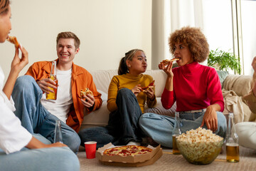 multiracial group of young people at house party eating pizza and drinking beer and having fun with friends