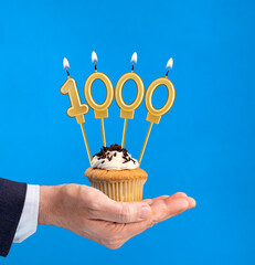 Hand delivering birthday cupcake - Candle number 1000 on blue background
