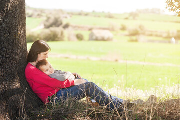 Mother and son relaxing in the shade of an oak tree next to some meadows. Tenderness, family. .