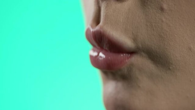 Makro zbliżenie ust i dłoni kobiety z r&oacute;żowymi paznokciami wkładającej malinę do ust i oblizującej wargi &mdash; zielonkawo-morskie tło, smak, slow motion 4K, kobiecy detal