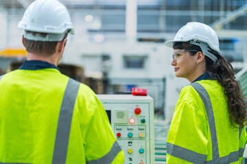 Male and female engineers in neat work clothes prepare and control the production system of large modern machines in a factory producing industrial technology products.