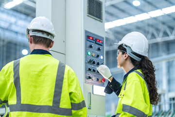 Male and female engineers in neat work clothes prepare and control the production system of large modern machines in a factory producing industrial technology products.