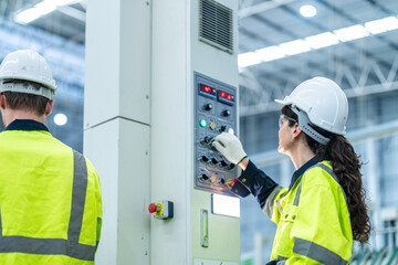 Male and female engineers in neat work clothes prepare and control the production system of large modern machines in a factory producing industrial technology products.