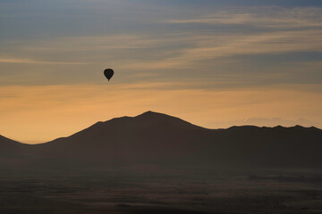 A single hot air balloon, sihouetted against the sun rise, as it floats above Morocco's Atlas mountians