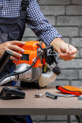  Technician, man in uniform is repairing a petrol mower on workbench. Small business.