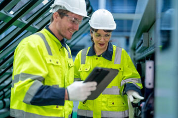 Male and female engineers in neat work clothes prepare and control the production system of large modern machines in a factory producing industrial technology products.