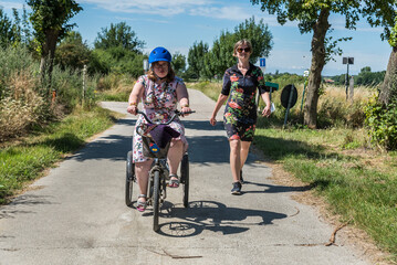 Young woman with Down syndrome on a tricycle and her friend in a dress driving through the fields...