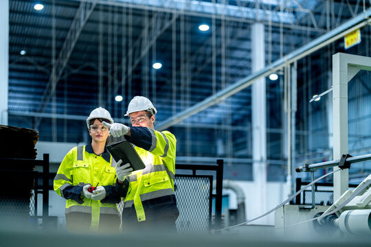 Male and female engineers in neat work clothes prepare and control the production system of large modern machines in a factory producing industrial technology products.